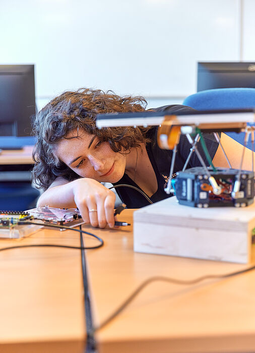 A young woman with dark hair holds a cable in her hand and wants to connect it to a technical device